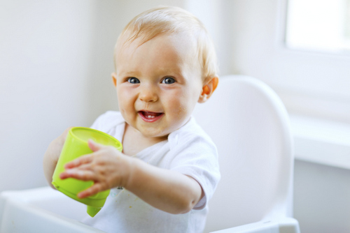 Baby girl holding sippy cup in a high chair after visit to Riverwind Dental in Richmond, VA