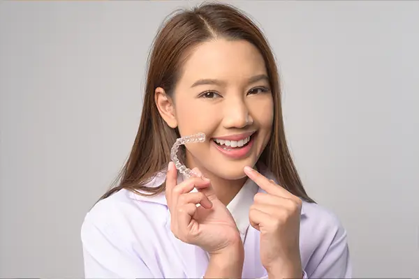 Young teen girl smiling and pointing at Invisalign clear aligners in hand at Riverwind Dental in Richmond, VA Young teen girl smiling and pointing at Invisalign clear aligners in hand at Riverwind Dental in Richmond, VA