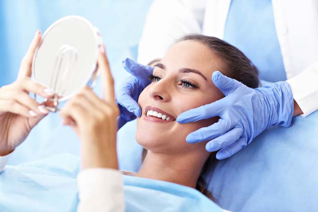 Woman in dental chair holding hand held mirror at Riverwind Dental in Richmond, VA