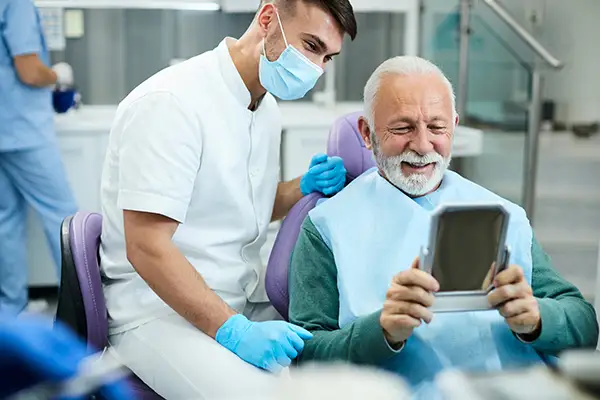 Happy, senior patient looking at himself in a mirror with his new dental implants at Riverwind Dental in Richmond, VA