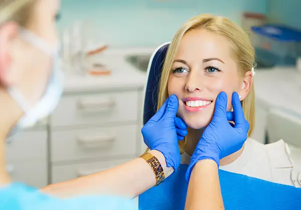A dentist wearing blue gloves checking a female patient's smile at Riverwind Dental in Richmond, VA