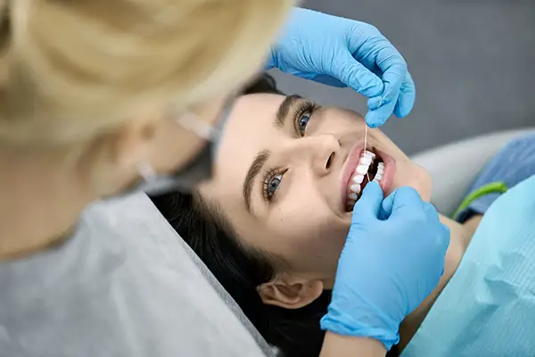 A hygienist flosses a female patient's newly cleaned teeth at the end of her dental visit.