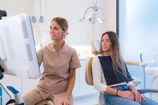 A dentist showing a female patient her dental X-ray results on a screen, discussing treatment options during an exam. A dentist showing a female patient her dental X-ray results on a screen, discussing treatment options during an exam.