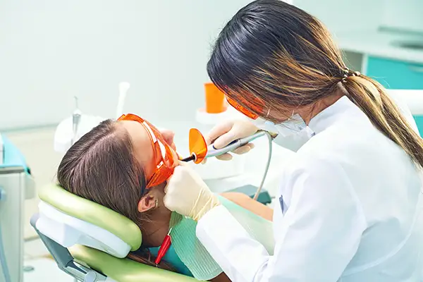 A dentist applying a dental sealant to a young patient's teeth using a curing light while the patient wears protective glasses at Riverwind Dental in Henrico, VA