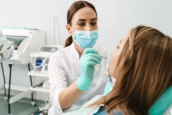 A dentist wearing a face mask examining a female patient's teeth at Riverwind Dental in Henrico, VA