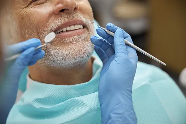 A dentist using dental tools to examine the teeth of an older male at Riverwind Dental in Henrico, VA A dentist using dental tools to examine the teeth of an older male at Riverwind Dental in Henrico, VA