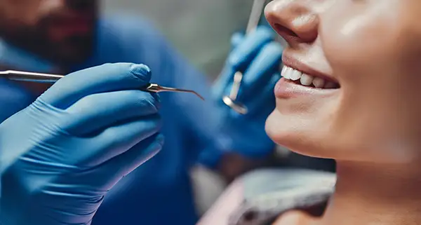 Close-up of a dental patient smiling while a dentist uses a mirror and scaler for a detailed examination at Riverwind Dental in Henrico, VA Close-up of a dental patient smiling while a dentist uses a mirror and scaler for a detailed examination at Riverwind Dental in Henrico, VA