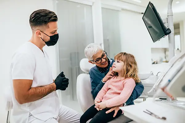 A cute little girl sitting in dentist chair before a routine dental procedure, accompanied by her grandmother at Riverwind Dental in Henrico, VA