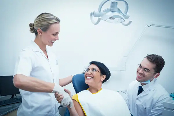 A woman smiling and shaking hands with her dentist at Riverwind Dental in Richmond, VA