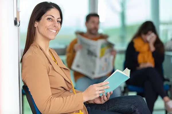 A smiling woman reading a book patiently while she waits for her dentist appointment at Riverwind Dental in Henrico, VA