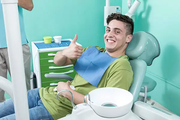 A grinning young man sitting in the dentist chair with a bib on at Riverwind Dental in Henrico, VA