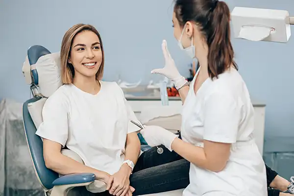 A smiling patient sits in a dental chair and listens while the dental hygienist welcomes her at Riverwind Dental in Henrico, VA