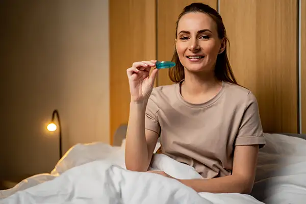 Woman sitting in bed holding a blue mouth guard from Riverwind Dental in Henrico, VA