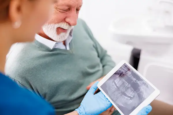 A dental assistant showing a digital x-ray to a senior patient on a tablet during a dental implant consultation at Riverwind Dental in Richmond, VA