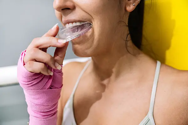 A female athlete putting on a sports guard before beginning her boxing training, in order to protect her teeth.