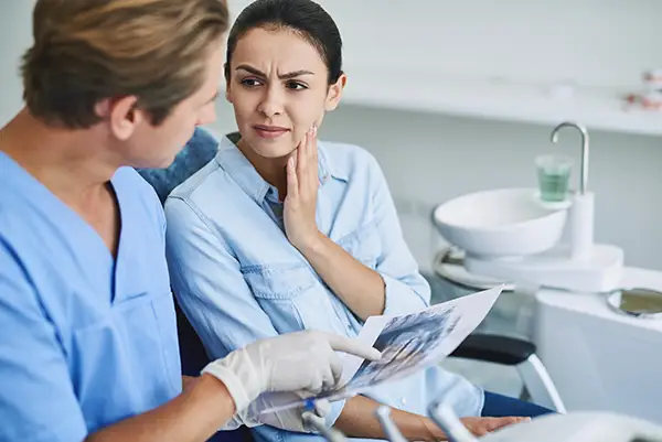 A dentist in scrubs discussing an X-ray with a female patient holding her jaw in pain at Riverwind Dental in Henrico, VA